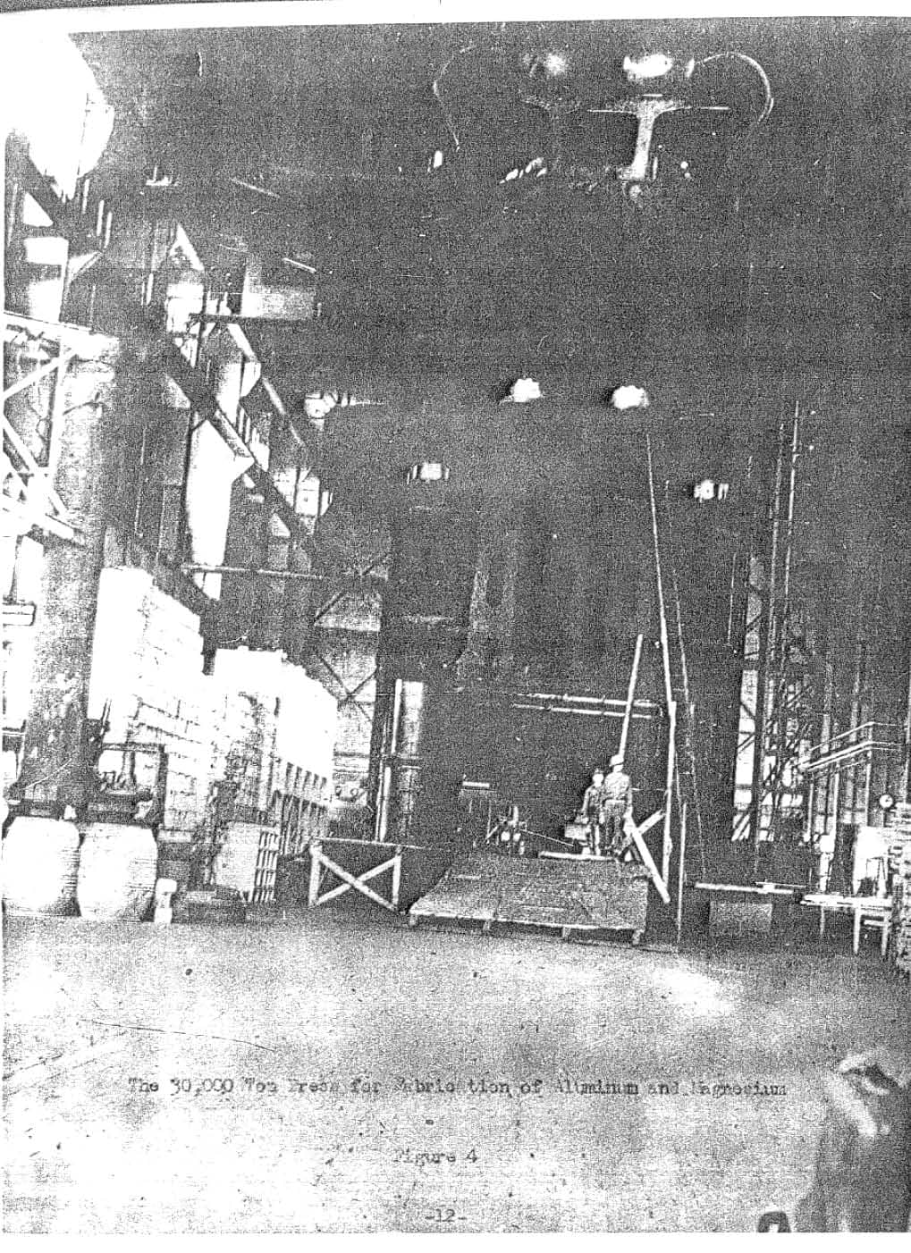 Poor photocopy of a photograph of the 30,000-ton press seen end-on in its hall, with two men standing on the press table and a typed caption below.